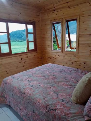a bedroom with a bed in a wooden room with windows at Cabana Caminho das Borboletas in Bom Retiro