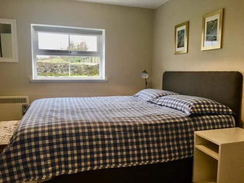 a bedroom with a bed with a plaid blanket and a window at Woodside Cottage Self Catering in Kinbuck