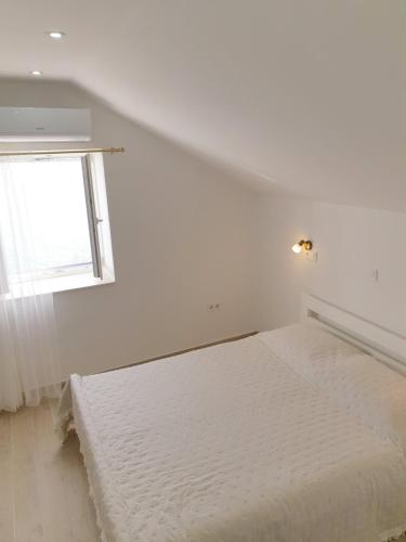 a white bedroom with a bed and a window at Rooms in Primošten