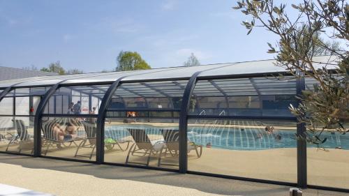 un pavillon en verre avec des chaises et une piscine dans l'établissement Camping Caravaning Les Cerisiers Berck sur mer, à Verton