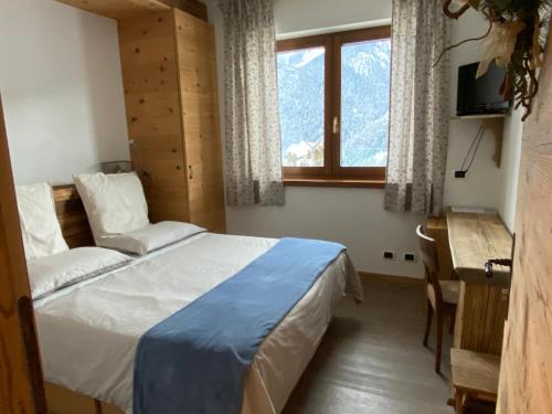 1 dormitorio con cama, escritorio y ventana en Fra Rose e Mughi, en Domegge di Cadore