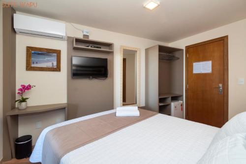 a bedroom with a large white bed and a tv at Pousada Kia Ora Bombinhas in Bombinhas