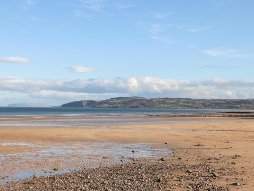 a beach with the ocean and mountains in the background at 4 Parc Delfryn in Llanallgo
