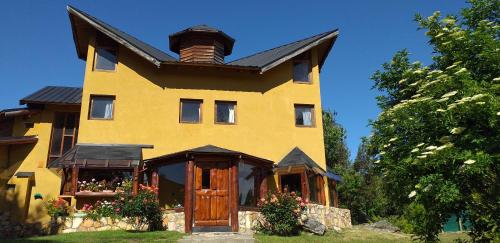 una gran casa amarilla con techo de gambrel en Ailín Maiá Apartamentos Casa de Montaña en San Carlos de Bariloche