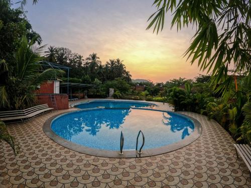 a swimming pool with a sunset in the background at Arthigamya Spa & Resort in Gokarna