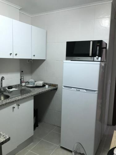 a white kitchen with a microwave on top of a refrigerator at Miguel Torga Typical in Coimbra