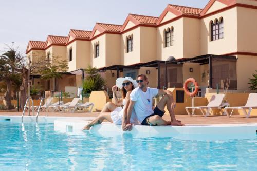 a man and a woman sitting on a surfboard in a swimming pool at Apartment Magica with Pool Fuerteventura Costa Calma in Costa Calma
