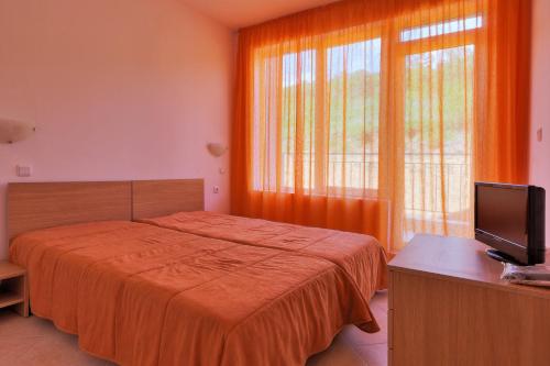 a bedroom with a bed with an orange blanket and a television at Sunset Complex in Kosharitsa