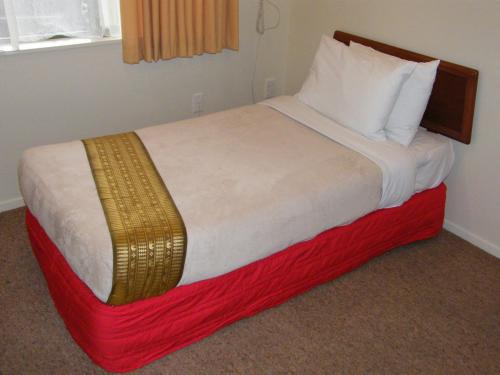 a bed in a hotel room with a red and white blanket at Hamilton Settlers Motor lodge in Hamilton