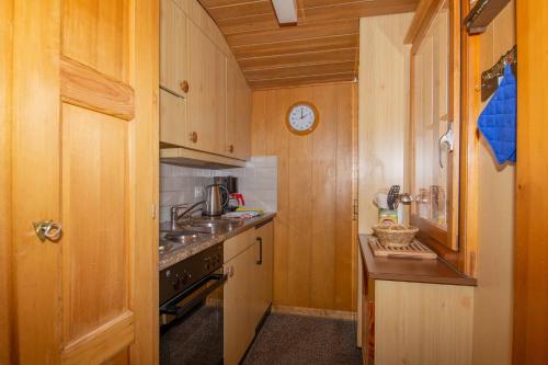 une cuisine avec des placards en bois et une horloge murale dans l'établissement Chalet Iris, à Adelboden