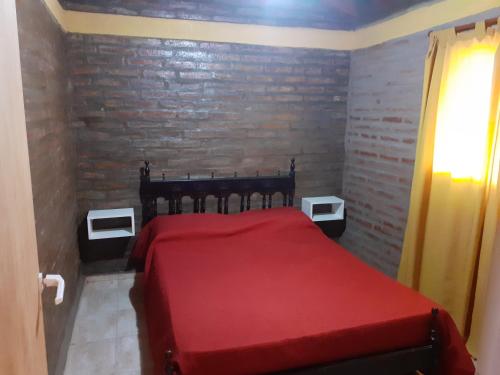 Una cama roja en una habitación con una pared de ladrillo en Jireh - Embalse en Embalse
