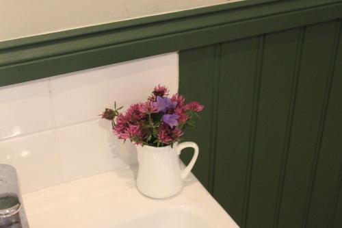 um vaso branco com flores em cima de um lavatório em Heatherbank Guest House em Strontian