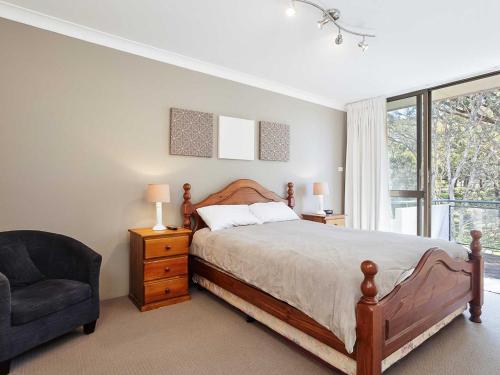 a bedroom with a bed and a chair and a window at Mistral Court 14 across the road from the beach in Nelson Bay