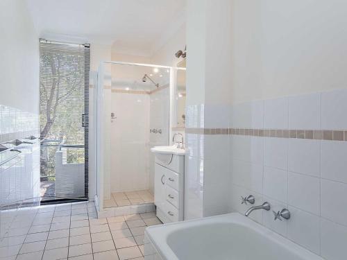 a white bathroom with a shower and a sink at Mistral Court 14 across the road from the beach in Nelson Bay