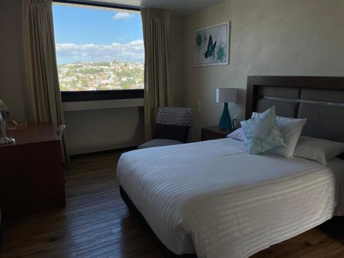 Tlaxcala de XicohténcatlにあるHotel Mirante Tlaxcalaのベッドと大きな窓が備わるホテルルームです。