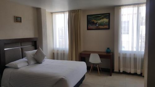 a bedroom with a bed and a desk and windows at Hotel Mirante Tlaxcala in Tlaxcala de Xicohténcatl