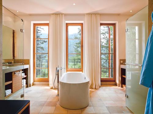 ein Bad mit einer großen Badewanne in einem Zimmer mit Fenstern in der Unterkunft Schloss Elmau Luxury Spa Retreat & Cultural Hideaway in Elmau