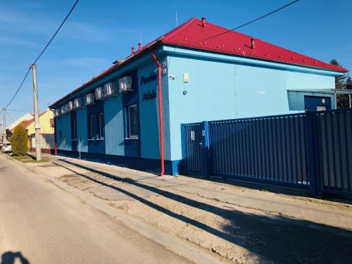 a blue building with a red roof next to a street at Penzión Pohoda in Nové Zámky