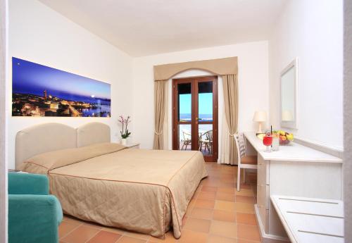 una camera con letto, scrivania e finestra di Hotel Punta Negra a Fertilia