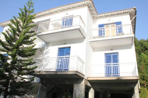 a white building with blue balconies and a pine tree at Theodora Studios in Yenion