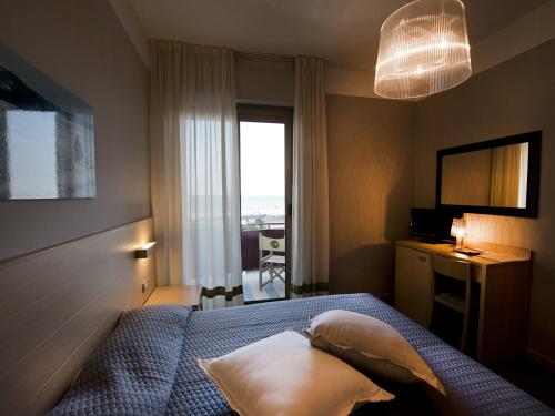 a bedroom with a bed and a desk and a window at Rouge Hotel International in Milano Marittima