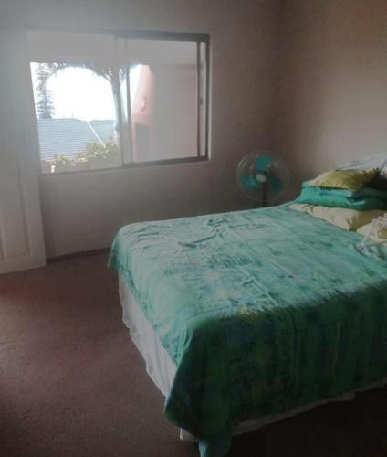 a bedroom with a bed with a green blanket and a window at Bona Manzi 7 in Hibberdene
