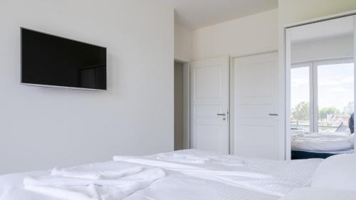 ein weißes Schlafzimmer mit einem Bett und einem Flachbild-TV in der Unterkunft Apartmenthaus Wittsande Wittsande 09 in Zingst