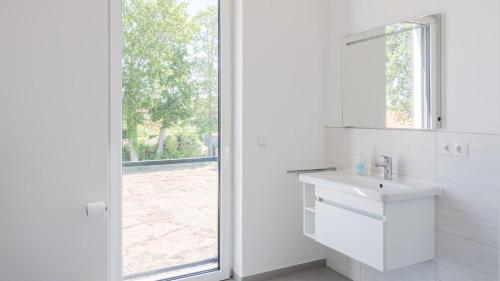 ein weißes Bad mit einem Waschbecken und einem Fenster in der Unterkunft Apartmenthaus Wittsande Wittsande 09 in Zingst