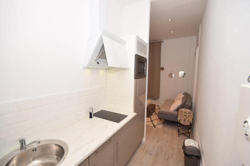 a white kitchen with a sink and a kitchen with a chair at CHIC APPART DESIGN - HYPER CENTRE - TRAMWAY - FREE WIFI - leRelaisdOdile12 in Valenciennes