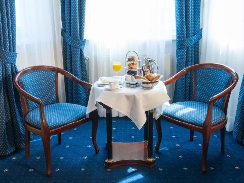 a table with two chairs and a table with a plate of food at Hotel Ambassador in Vienna