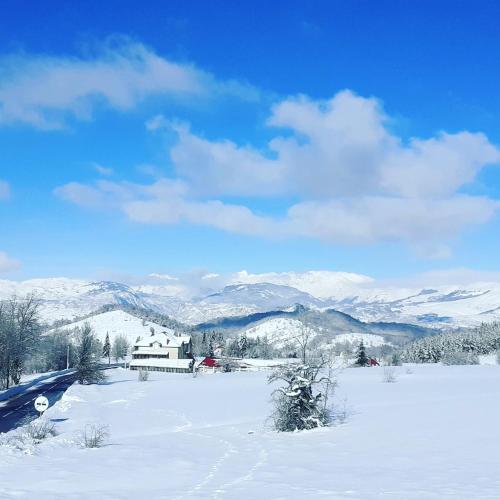 a snow covered field with a house and mountains at Romantika in Šavnik