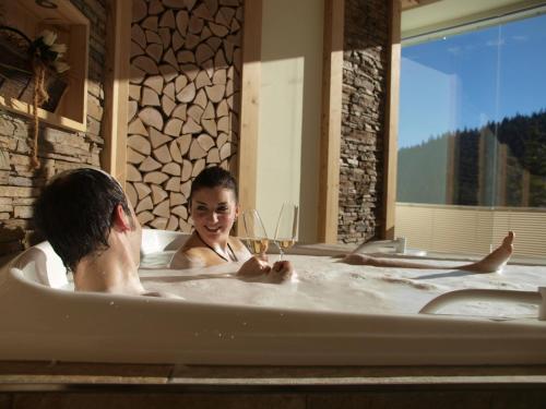 Das Waldhotel - Genuss & Wellness am Notschreipass في تودتناو: شخصان في حوض استحمام مع كأس من النبيذ