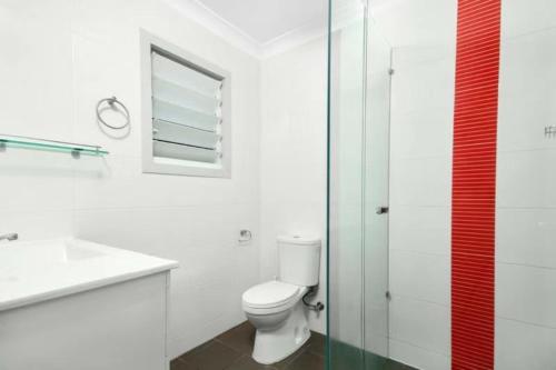 a white bathroom with a toilet and a glass shower at Martyn st house in Cairns