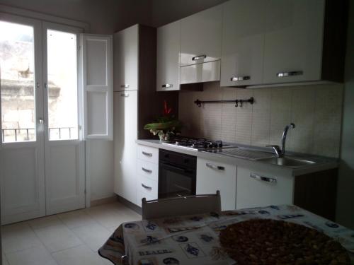 cocina con armarios blancos, fregadero y mesa en La Casa Delle Conchiglie, en Trapani