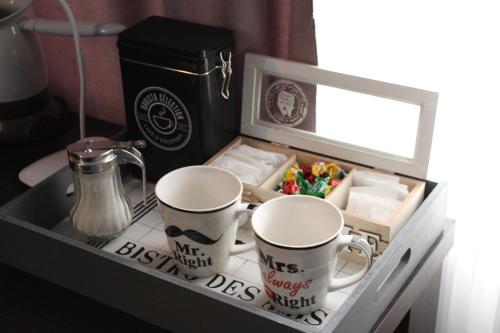 a tray with two coffee mugs and a box of sweets at Apartman Daca in Podgorica