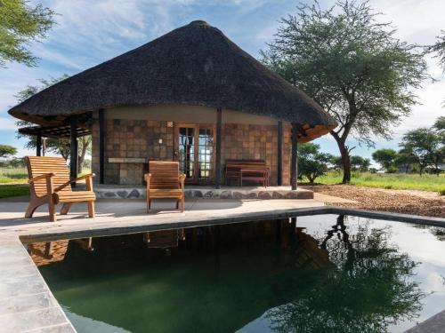 a hut with two chairs and a swimming pool at Africa Awaits Lodge & Safaris in Gobabis