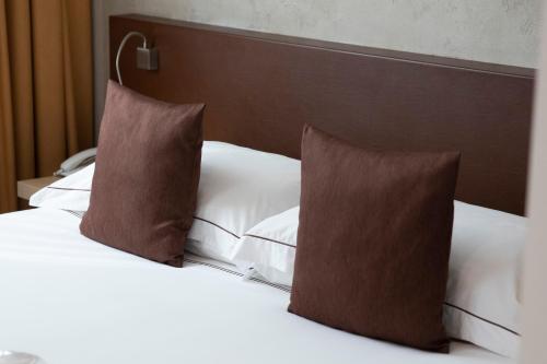 a bed with white sheets and brown pillows at Airporthotel Verona Congress & Relax in Dossobuono