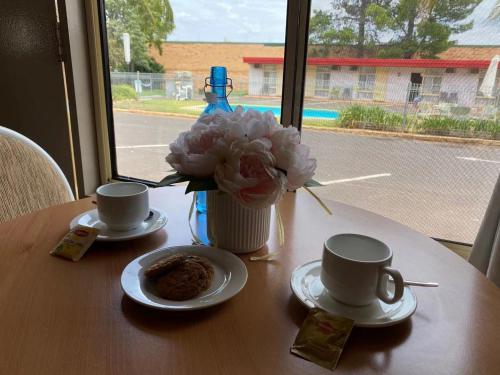 a table with two cups and a vase of flowers at Apollo Motel Parkes in Parkes