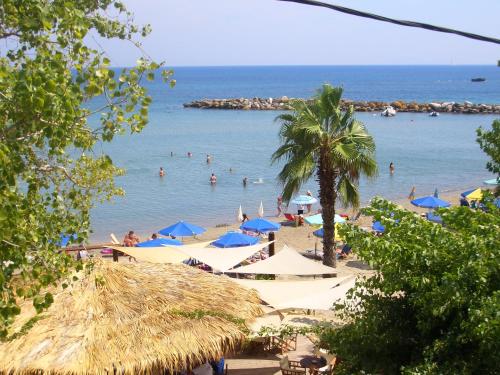 a beach with people in the water and blue umbrellas at Hercules Sea Front Studios in Katelios