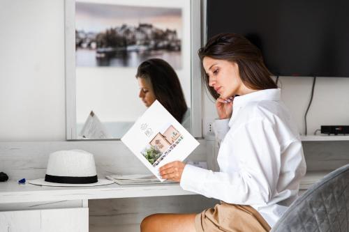 a woman sitting on a desk reading a book at Hotel RIO VERDE in Podgorica