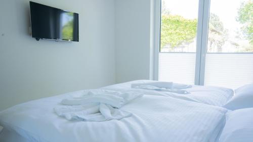 a white bed with white sheets and a tv on the wall at Haus am Dünenwald - Düne 1 in Zingst