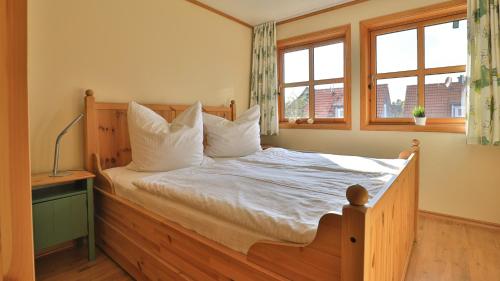 1 dormitorio con cama de madera y almohadas blancas en Heideröschen Park - Haus 5a, en Zingst