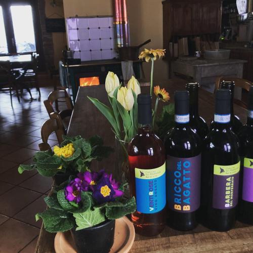 a table with three bottles of wine and flowers at Cascina La Maddalena Bed & Wine in Rocca Grimalda