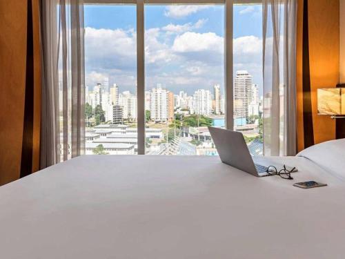 a laptop sitting on a bed with a large window at FLAT Jardins São Paulo excelente! in Sao Paulo