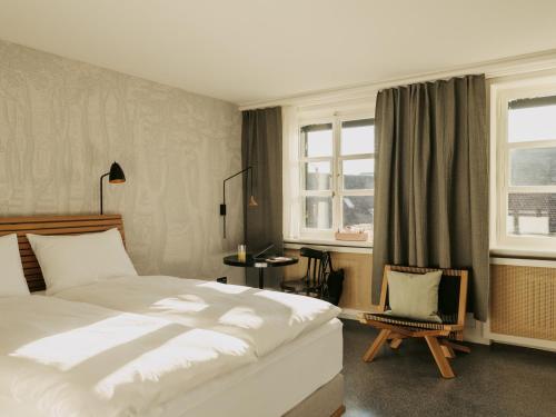 a bedroom with a bed and a chair and windows at Boutique & Design Hotel Volkshaus Basel in Basel