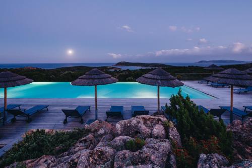 a swimming pool with umbrellas and chairs and the ocean at Résidence Les Terrasses de Rondinara in Bonifacio