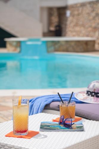 two glasses sitting on a table next to a swimming pool at Lu' Hotel Maladroxia in SantʼAntìoco