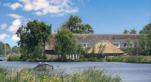 a large house with a thatched roof in front of a lake at Groeten uit Hoogmade - rural cottage in Hoogmaden
