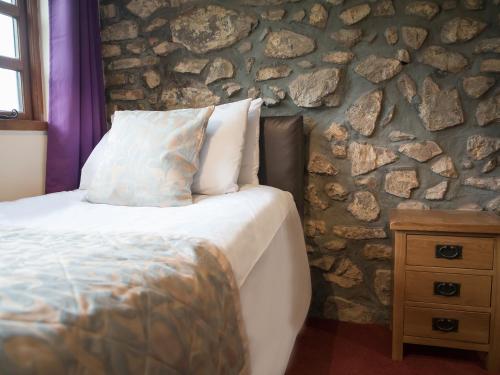 a bedroom with a bed and a stone wall at Brambles Cottage in Great Malvern