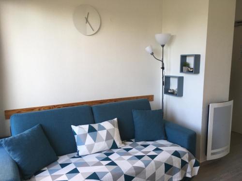 - un canapé bleu dans une chambre avec une horloge sur le mur dans l'établissement Cabourg, T2 parfait pour vous ! Proche plage et centre-ville, 2 à 4 pers., à Cabourg